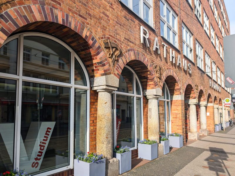 Fassade des Rathauses mit großen Fenstern und Pflanzkästen aus Stein im Vordergrund.